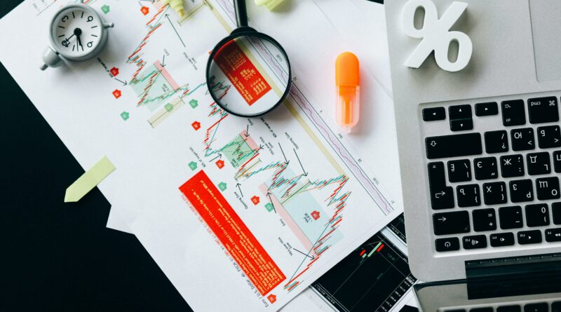 Top view of a desk with a laptop, percentage symbol, graphs, and magnifying glass used as a visualization of the numbers and data needed for SR&ED tax incentive program Image retrieved from pexels-nataliya-vaitkevich-6120214
